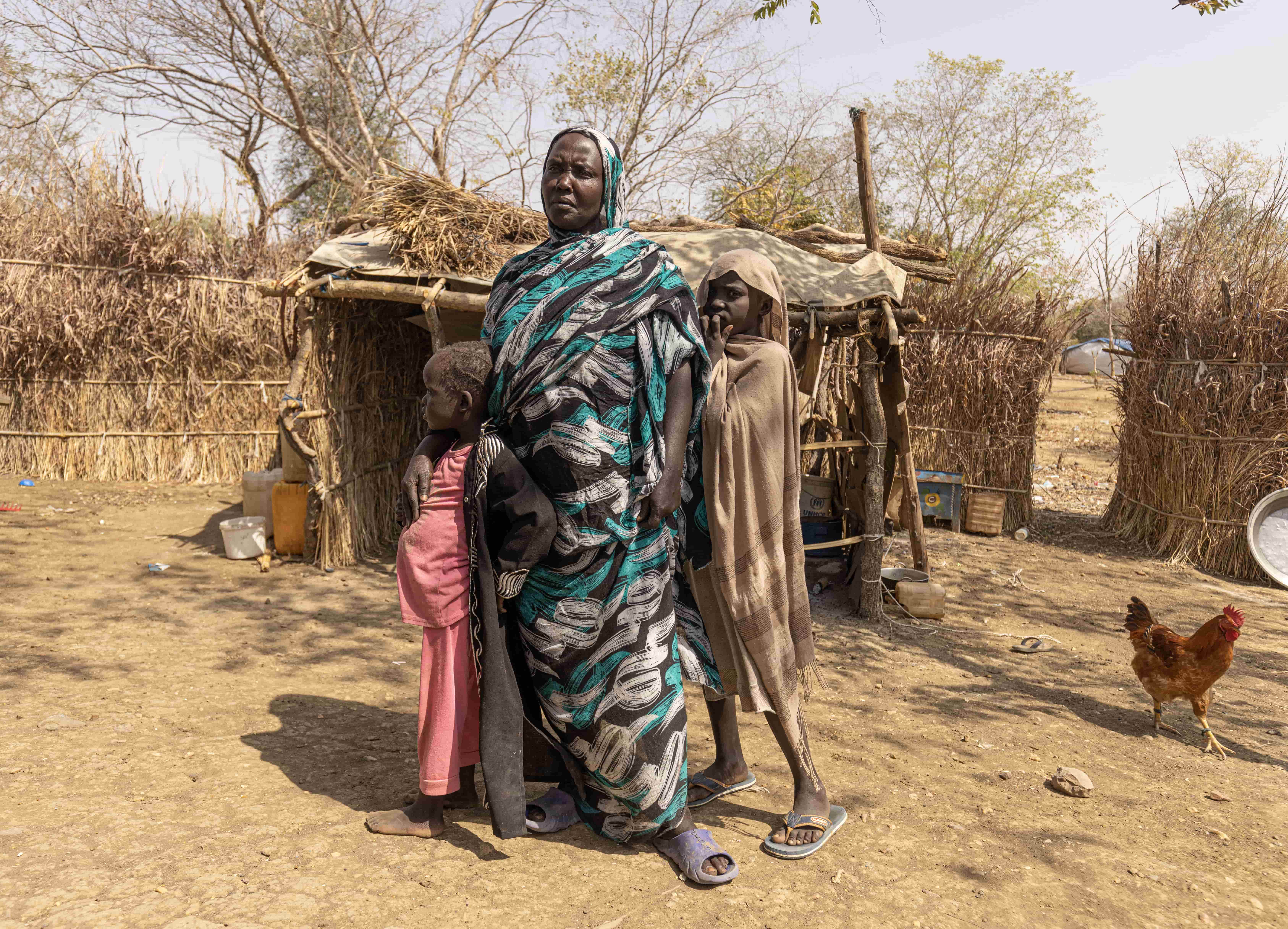 Hawa, 40, and her daughters Islam, 7, and Maha, 10, stand in front of their shelter at the Kurmuk transit centre, Ethiopia.