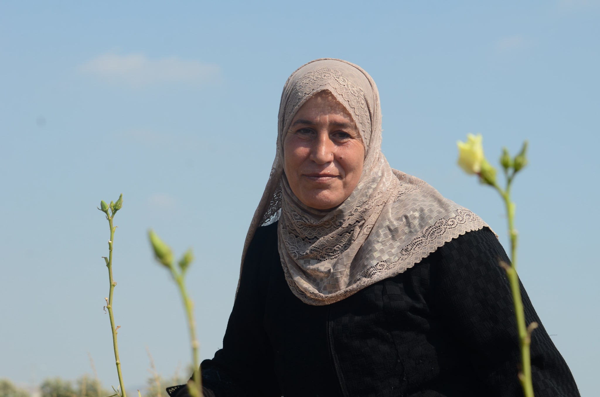 Portrait of Syrian refugee Layla amongst okra flowers. 