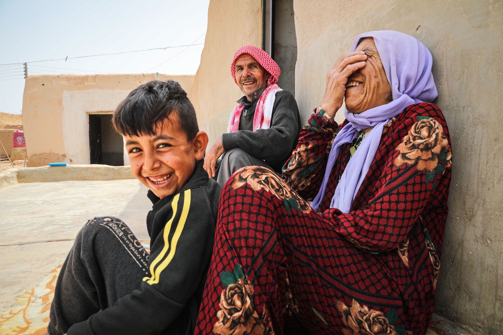 Shahada Al-Daais, 65, sits with his wife and son outside their repaired home in rural southern Aleppo, smiling after receiving UNHCR shelter support