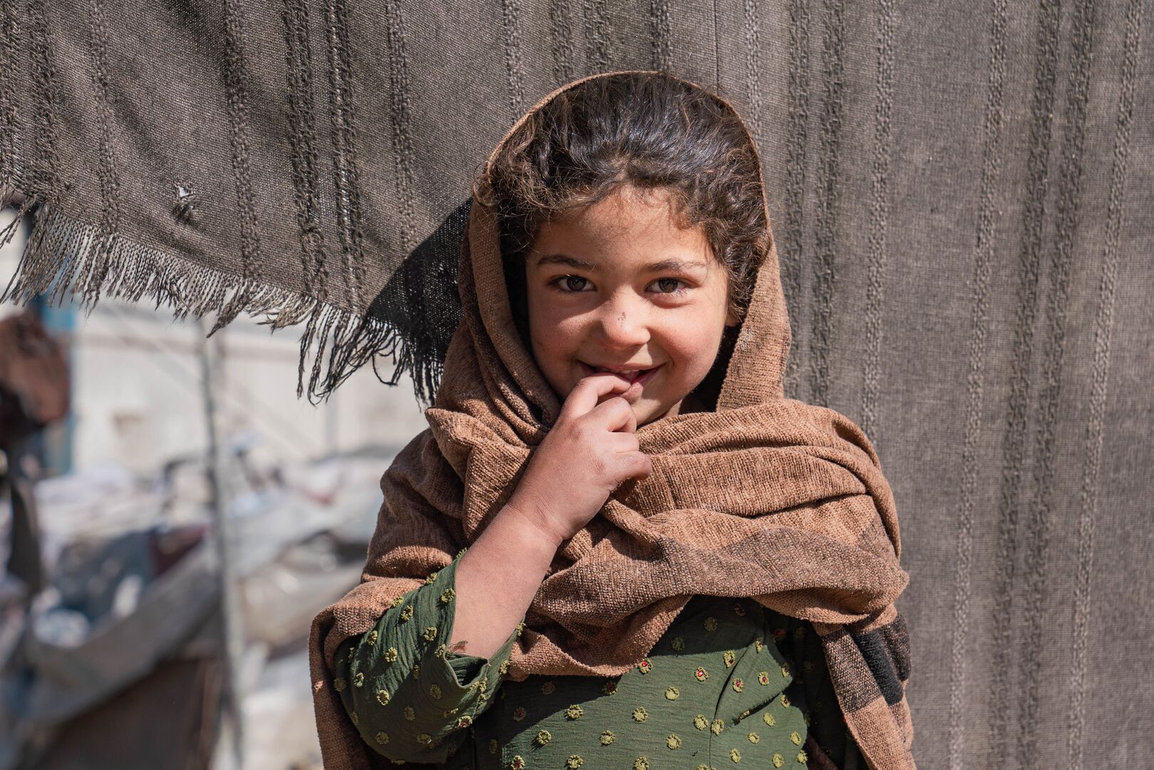 Nilofar, 6, stands outside her family’s tent in an informal settlement, looking into the camera and smiling