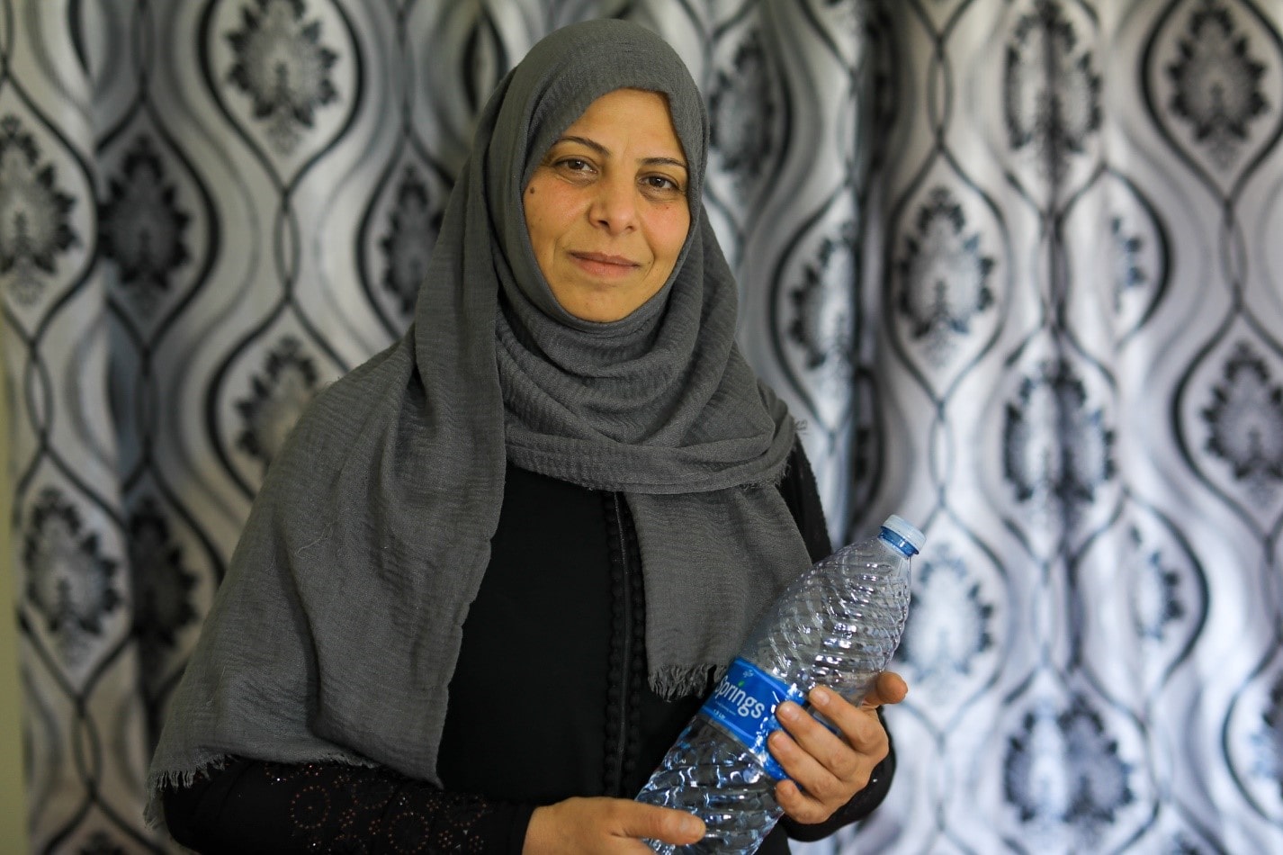 Syrian refugee Huda holds water bottle